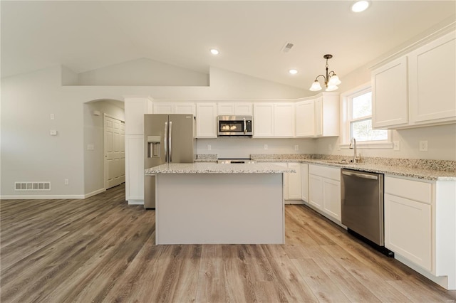 kitchen with lofted ceiling, hanging light fixtures, appliances with stainless steel finishes, and light hardwood / wood-style flooring