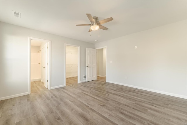 unfurnished bedroom featuring a spacious closet, a closet, ceiling fan, and light hardwood / wood-style flooring