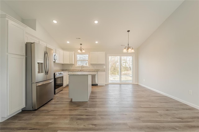 kitchen featuring a center island, light hardwood / wood-style floors, lofted ceiling, white cabinets, and appliances with stainless steel finishes