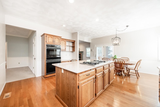 kitchen with hanging light fixtures, light hardwood / wood-style flooring, double oven, stainless steel gas stovetop, and a kitchen island