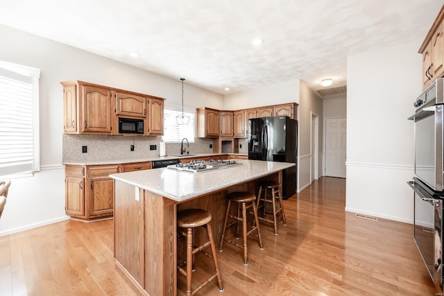 kitchen featuring a center island, black appliances, hanging light fixtures, light wood-type flooring, and tasteful backsplash