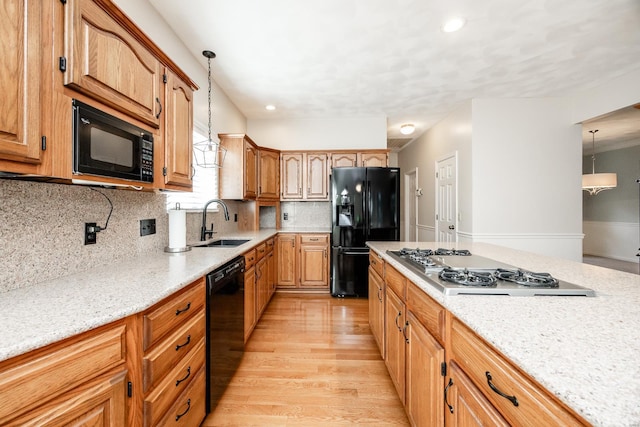 kitchen featuring pendant lighting, black appliances, sink, decorative backsplash, and light wood-type flooring