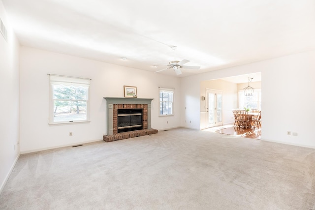 unfurnished living room with ceiling fan with notable chandelier, light carpet, and a brick fireplace