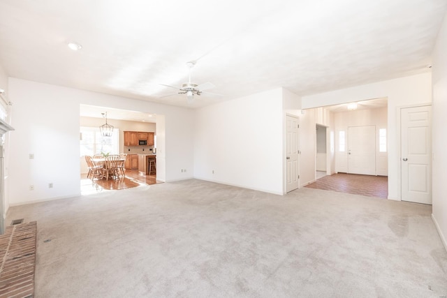 unfurnished living room featuring light carpet and ceiling fan with notable chandelier