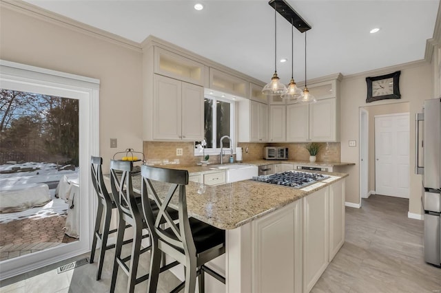 kitchen with a kitchen bar, sink, hanging light fixtures, appliances with stainless steel finishes, and light stone countertops