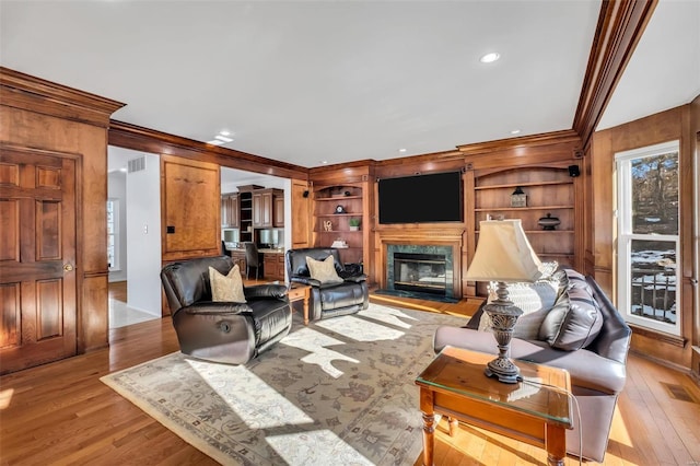 living room with built in shelves, crown molding, and light wood-type flooring