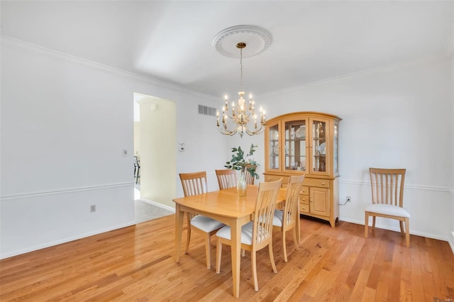 dining room with crown molding, an inviting chandelier, and light hardwood / wood-style floors