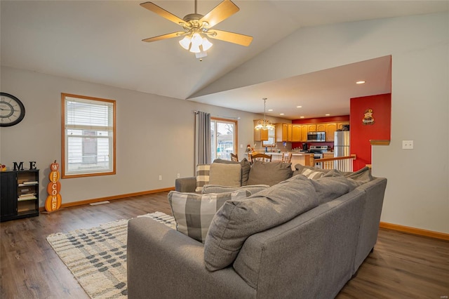 living room with a wealth of natural light, dark hardwood / wood-style flooring, ceiling fan with notable chandelier, and vaulted ceiling