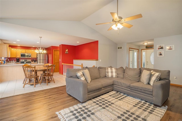 living room featuring ceiling fan with notable chandelier, light hardwood / wood-style floors, vaulted ceiling, and sink