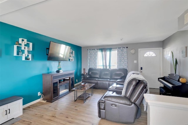 living area featuring a glass covered fireplace, baseboards, and light wood-style floors