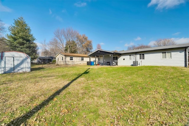 back of property featuring an outbuilding, central air condition unit, a lawn, and fence