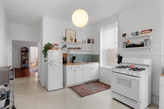 kitchen with white appliances, white cabinets, sink, hanging light fixtures, and plenty of natural light