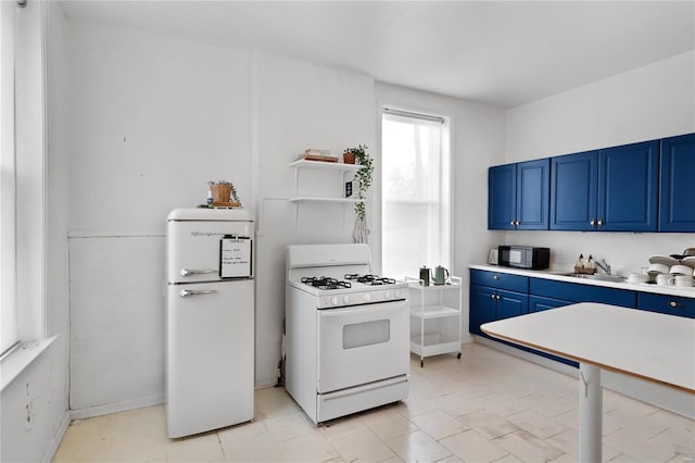 kitchen with refrigerator, blue cabinets, sink, light tile patterned floors, and gas range gas stove