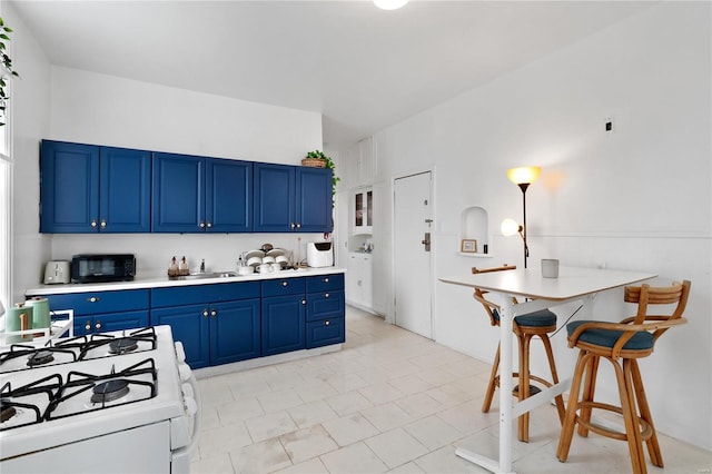 kitchen featuring blue cabinetry, white gas stove, a kitchen bar, and sink