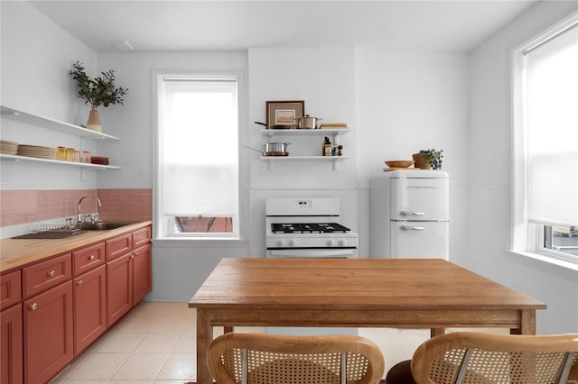 kitchen featuring tasteful backsplash, white range, sink, light tile patterned floors, and fridge