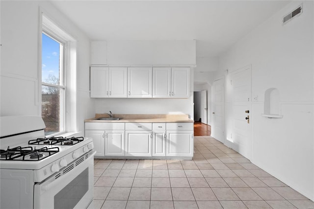 kitchen featuring white range with gas stovetop, light tile patterned floors, white cabinets, and sink