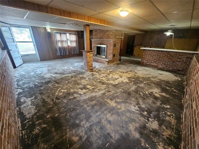 basement with a fireplace, a drop ceiling, and brick wall