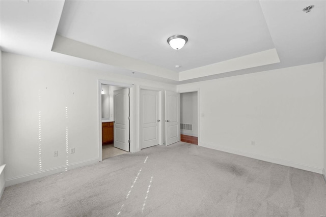 unfurnished bedroom with a tray ceiling, visible vents, light carpet, and baseboards