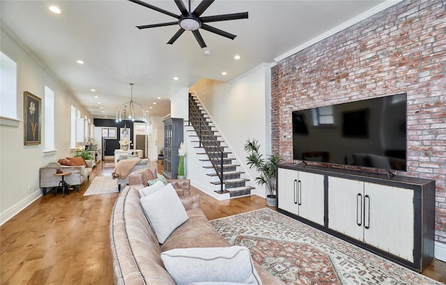 living room featuring ceiling fan with notable chandelier, light hardwood / wood-style flooring, crown molding, and brick wall