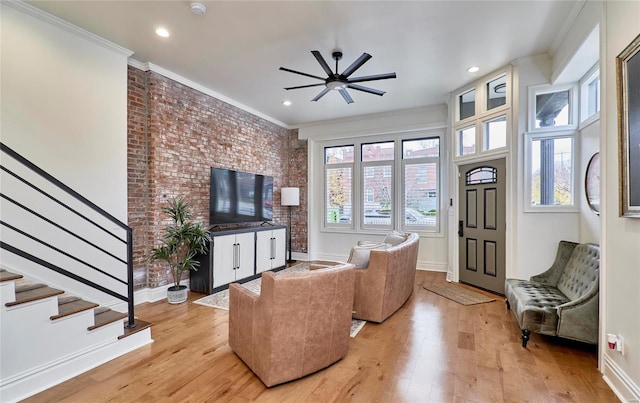 living room featuring light hardwood / wood-style floors, ceiling fan, crown molding, and brick wall