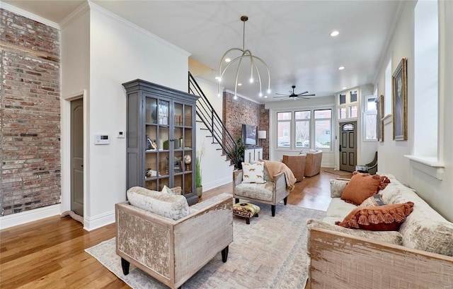 living room with ceiling fan with notable chandelier, hardwood / wood-style flooring, ornamental molding, and brick wall