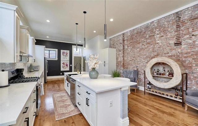 kitchen featuring pendant lighting, crown molding, light wood-type flooring, an island with sink, and appliances with stainless steel finishes