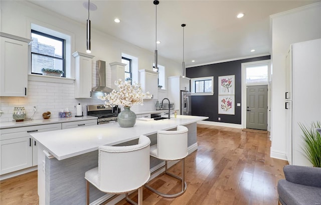 kitchen with wall chimney exhaust hood, a center island with sink, stainless steel stove, and pendant lighting