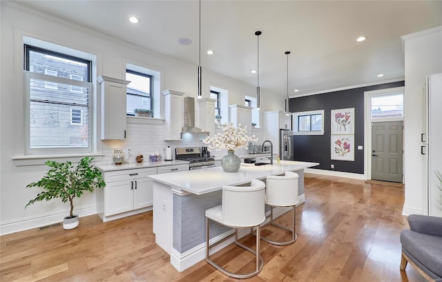 kitchen with white cabinetry, light hardwood / wood-style flooring, pendant lighting, a center island with sink, and appliances with stainless steel finishes