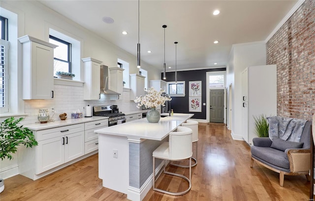 kitchen with light wood-type flooring, ornamental molding, decorative light fixtures, stainless steel range with gas cooktop, and an island with sink