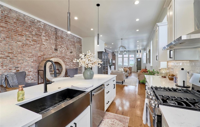 kitchen featuring wall chimney range hood, white cabinets, stainless steel appliances, and decorative light fixtures