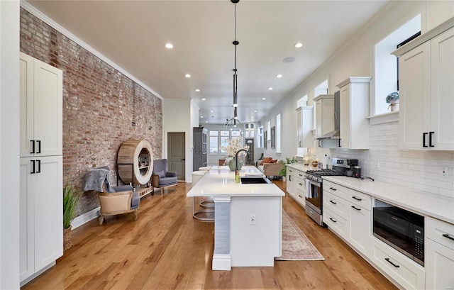 kitchen featuring pendant lighting, a kitchen island with sink, light hardwood / wood-style flooring, stainless steel gas range, and black microwave