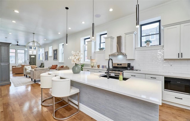 kitchen featuring a kitchen breakfast bar, wall chimney range hood, hanging light fixtures, ceiling fan, and white cabinetry