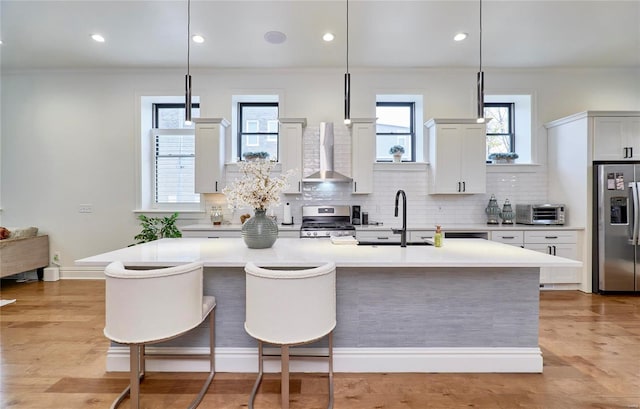 kitchen featuring a kitchen island with sink, wall chimney exhaust hood, hanging light fixtures, and appliances with stainless steel finishes