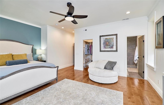 bedroom featuring a walk in closet, crown molding, ensuite bath, hardwood / wood-style flooring, and ceiling fan