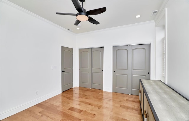 unfurnished bedroom with multiple closets, ceiling fan, crown molding, and light hardwood / wood-style floors