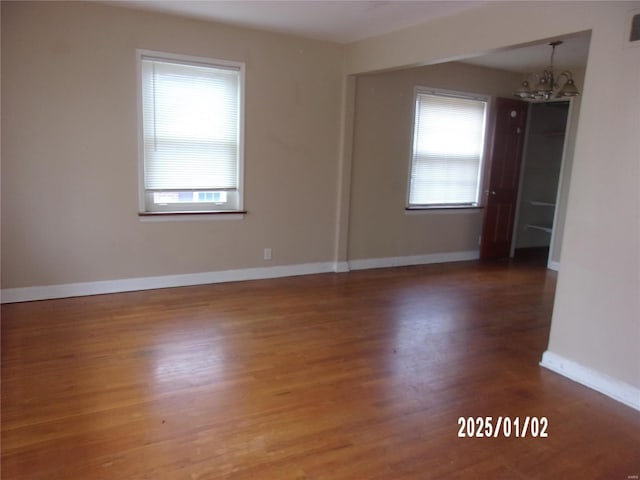 empty room featuring a healthy amount of sunlight, baseboards, an inviting chandelier, and wood finished floors