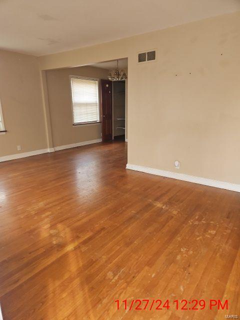 spare room featuring an inviting chandelier, wood finished floors, visible vents, and baseboards