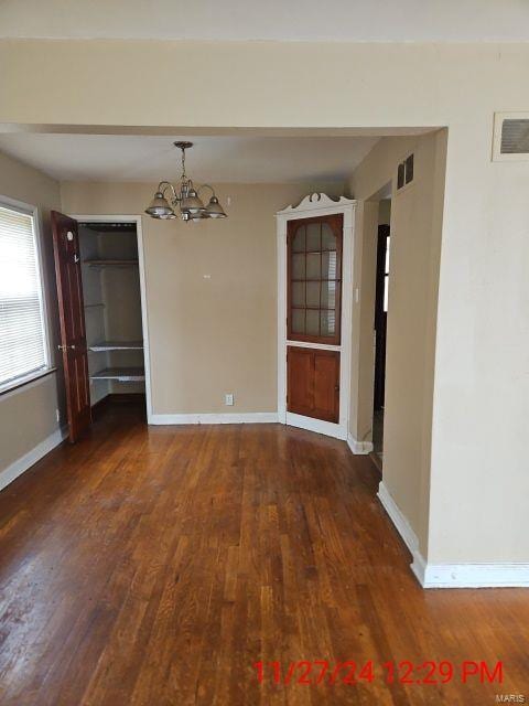 unfurnished dining area with a notable chandelier and dark wood-type flooring