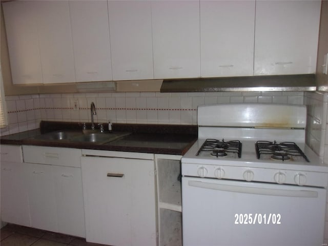 kitchen featuring dark countertops, white gas range oven, decorative backsplash, white cabinetry, and a sink