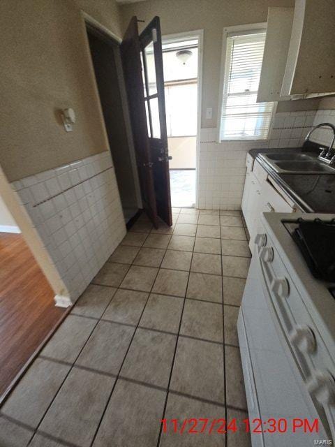 kitchen featuring tile walls, light tile patterned floors, wainscoting, white cabinetry, and a sink