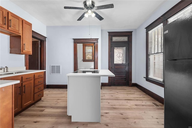 kitchen featuring a center island, black fridge, sink, light hardwood / wood-style flooring, and ceiling fan