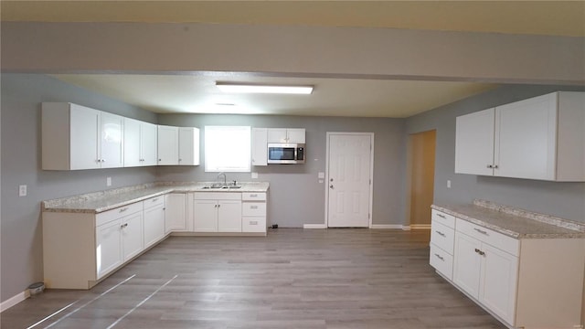 kitchen featuring white cabinetry, sink, light stone counters, and light hardwood / wood-style flooring