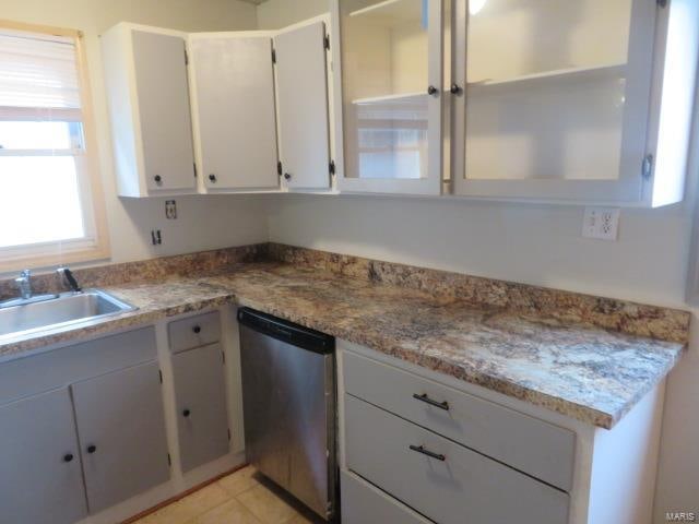 kitchen with light stone countertops, light tile patterned flooring, stainless steel dishwasher, and sink