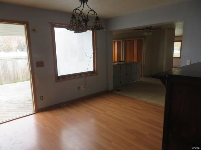 unfurnished dining area featuring ceiling fan with notable chandelier and light hardwood / wood-style flooring