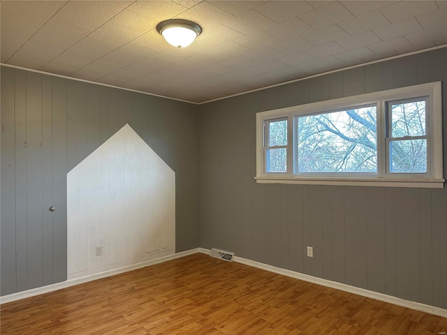 spare room with light wood-type flooring and wooden walls