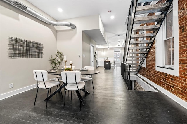 dining space featuring dark wood-type flooring and brick wall