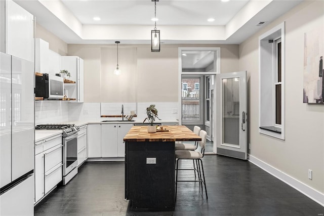 kitchen with butcher block counters, white cabinetry, a center island, pendant lighting, and white appliances