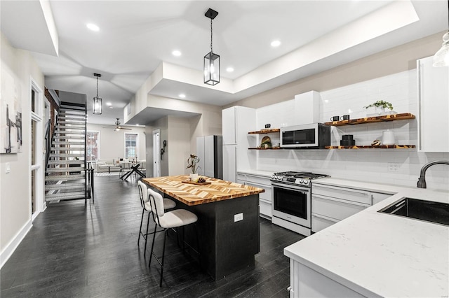 kitchen featuring a center island, sink, hanging light fixtures, stainless steel gas stove, and white cabinetry