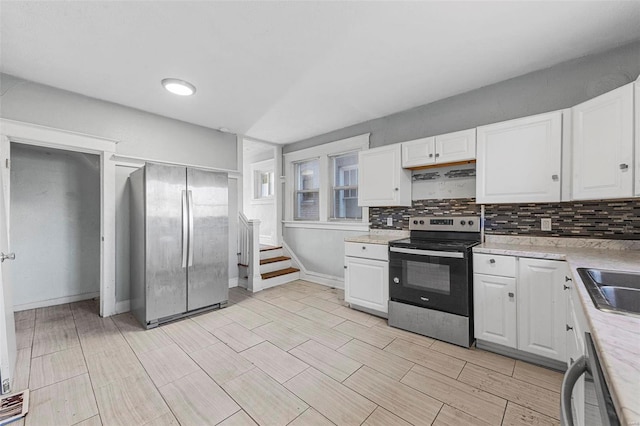 kitchen featuring white cabinets, decorative backsplash, range hood, and appliances with stainless steel finishes