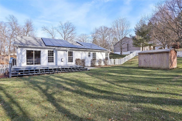 back of house featuring a deck, a lawn, a shed, and solar panels